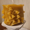 Yellow wax candle with a unique texture on a white stand against a neutral background