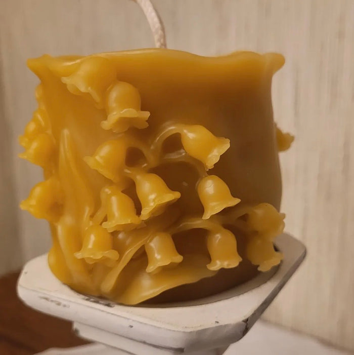 Yellow wax candle with a unique texture on a white stand against a neutral background