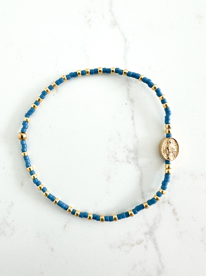 Blue beaded bracelet with gold accents on a white marble surface