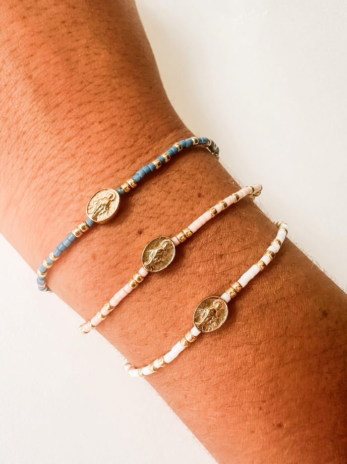 Three bracelets on a wrist with a plain background