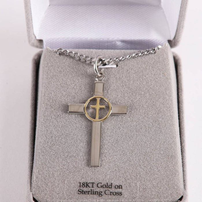 Silver cross pendant with gold circle on a chain in an open jewelry box.