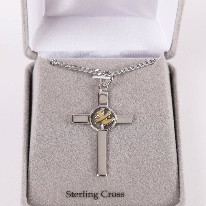 Silver cross pendant with a gold emblem on a gray cushion in a jewelry box.