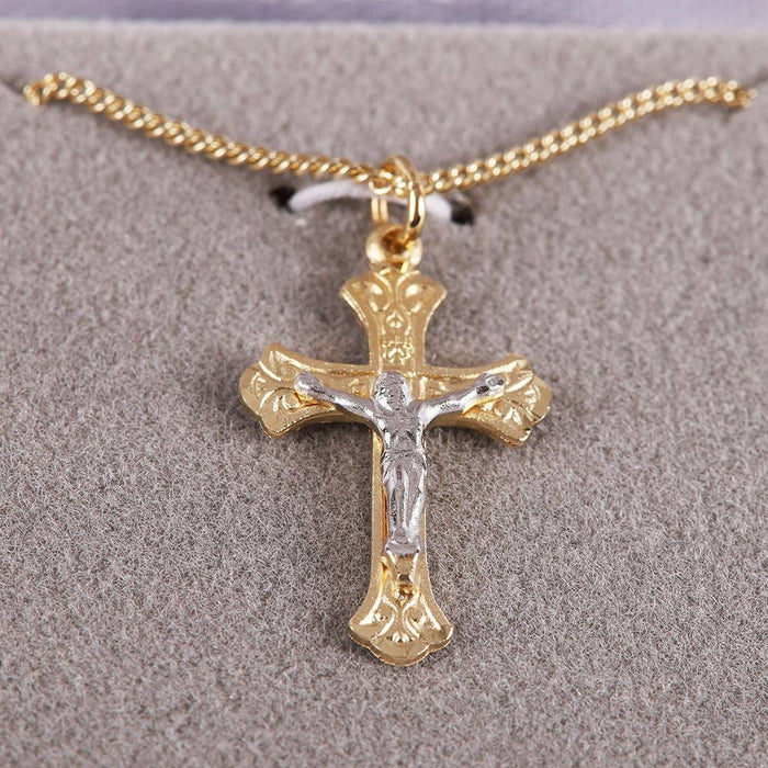 Gold and silver crucifix pendant on a chain against a gray background