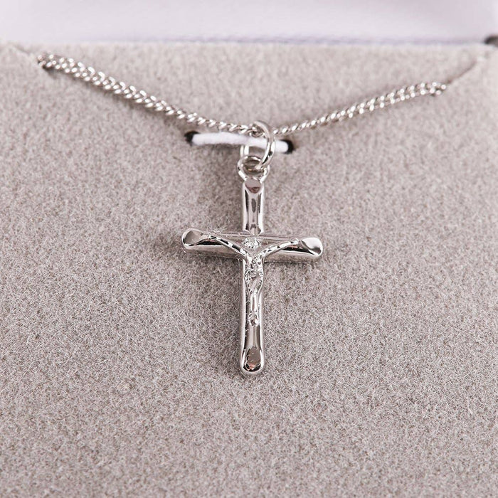 Silver cross pendant necklace on a textured beige surface