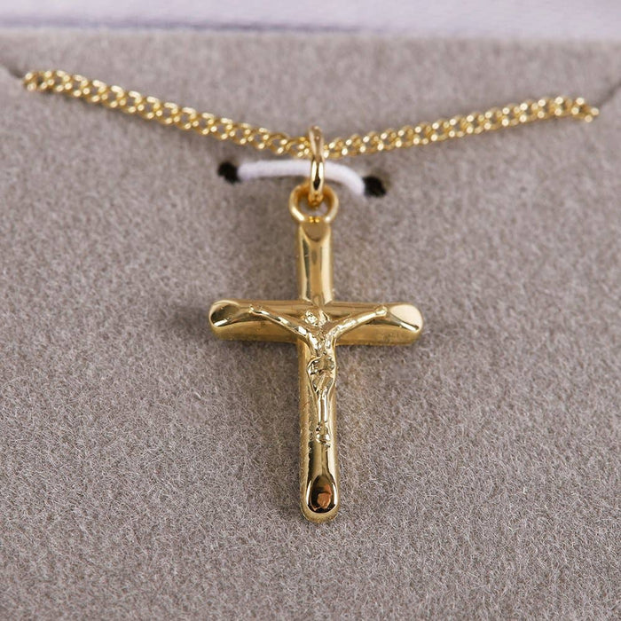 Gold crucifix pendant on a gold chain against a gray background