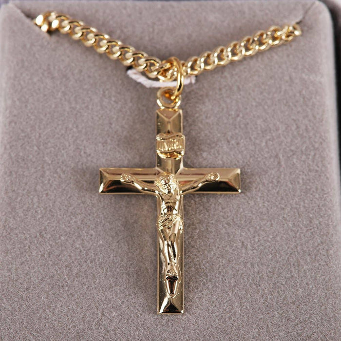 Gold crucifix pendant on a gold chain against a gray background