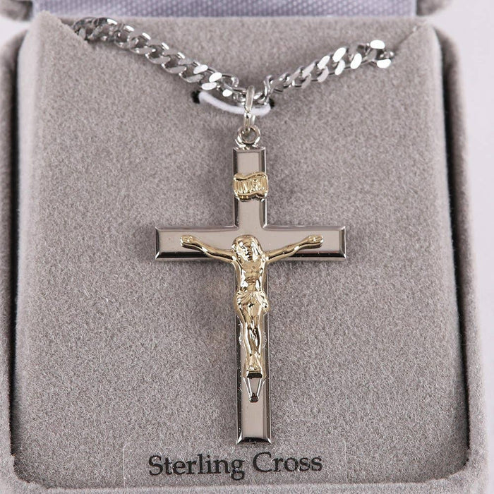 Silver crucifix necklace with gold accents on a gray cushion