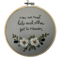 Embroidery hoop with text 'now we must help each other get to Heaven' and floral design on a gray background.