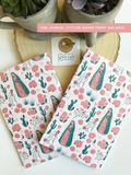 Two patterned journals with cactus and floral design on a wooden surface with plants.