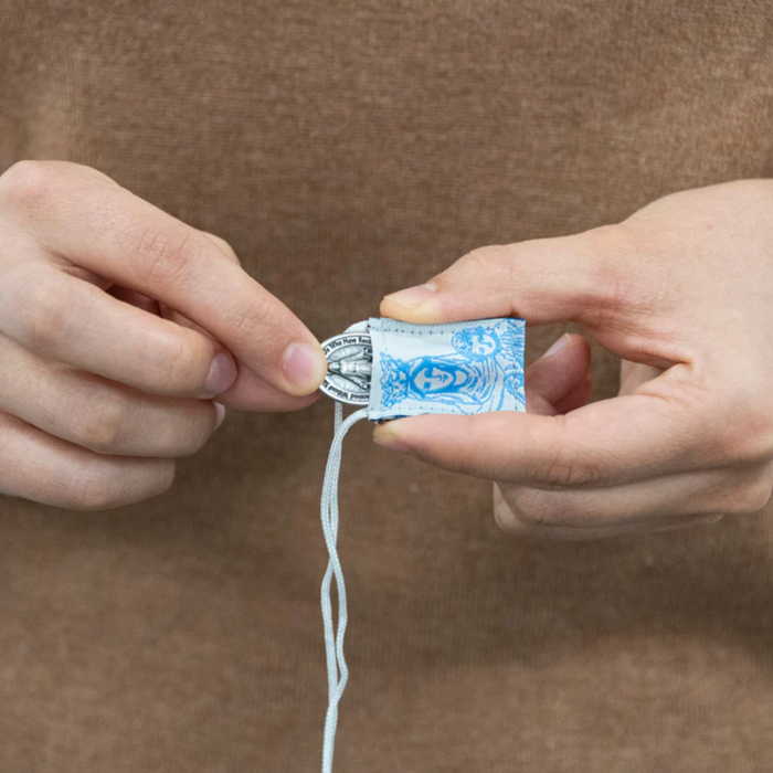 Person holding a small scapular with a blue our lady against a brown background