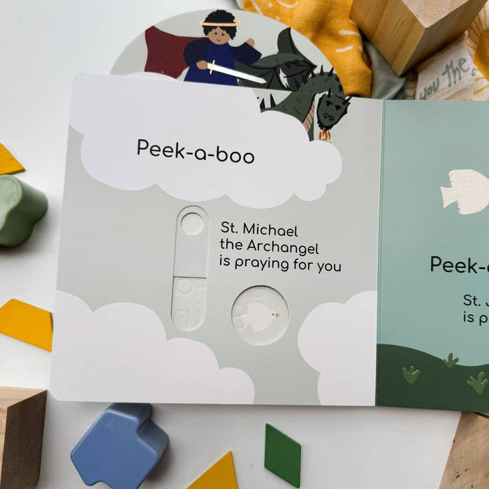 Children's book with a peek-a-boo feature featuring St. Michael the Archangel on a white surface with toys.