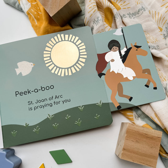 Children's book with illustrations of a sun, bird, and person on a horse, surrounded by wooden blocks and fabric.