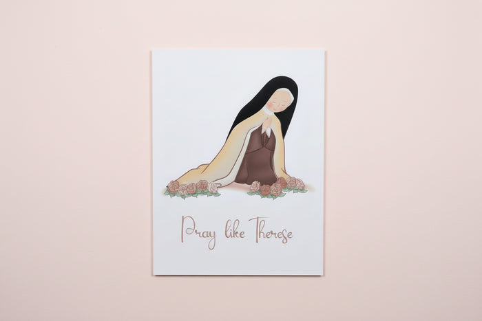 Print with illustration of st. Therese and text 'Pray like Therese' on a white surface.