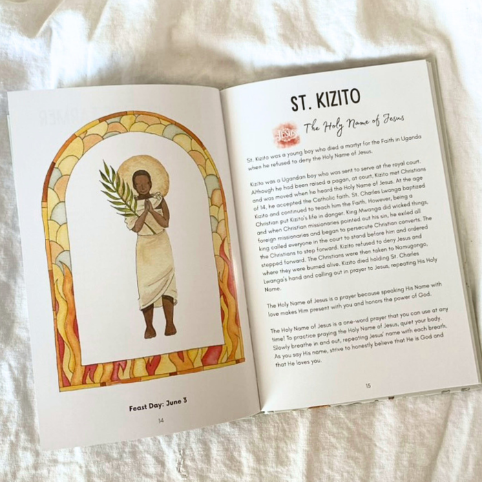 Open book with illustration of St. Kizito and text on a white fabric background