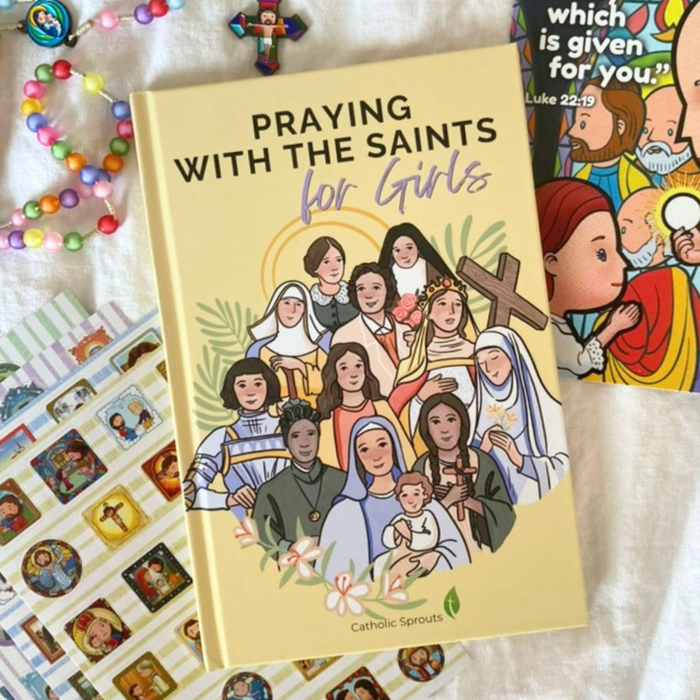 Book titled 'Praying with the Saints for Girls' on a white surface with religious items.