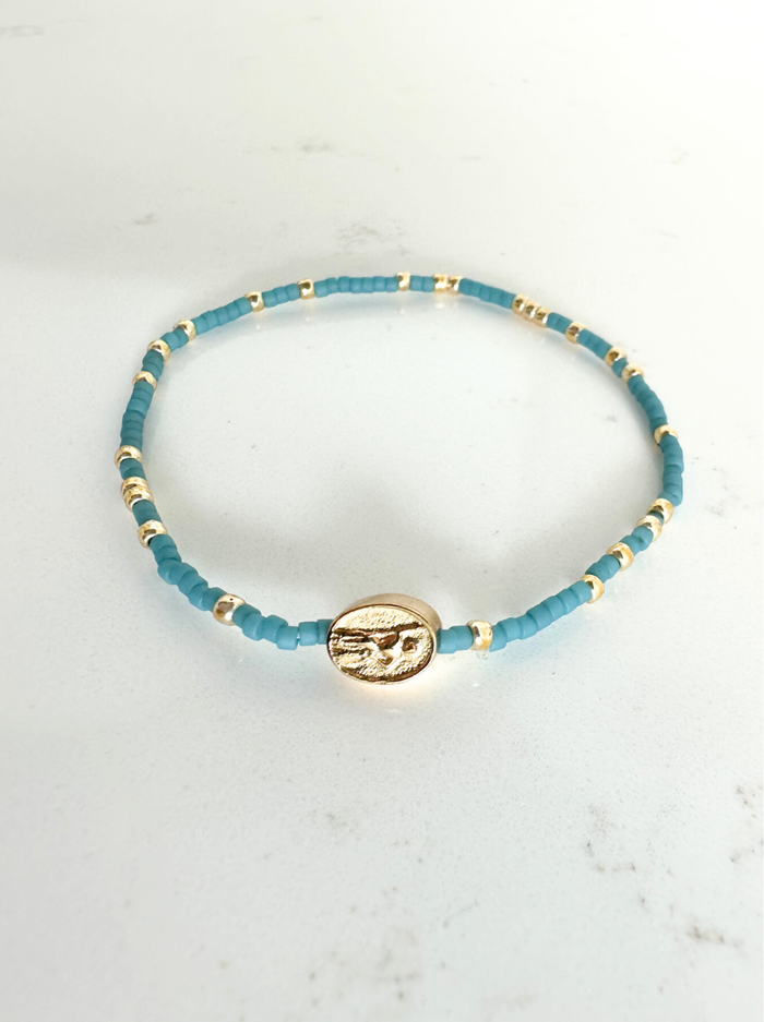 Blue beaded bracelet with a gold charm on a white marble surface