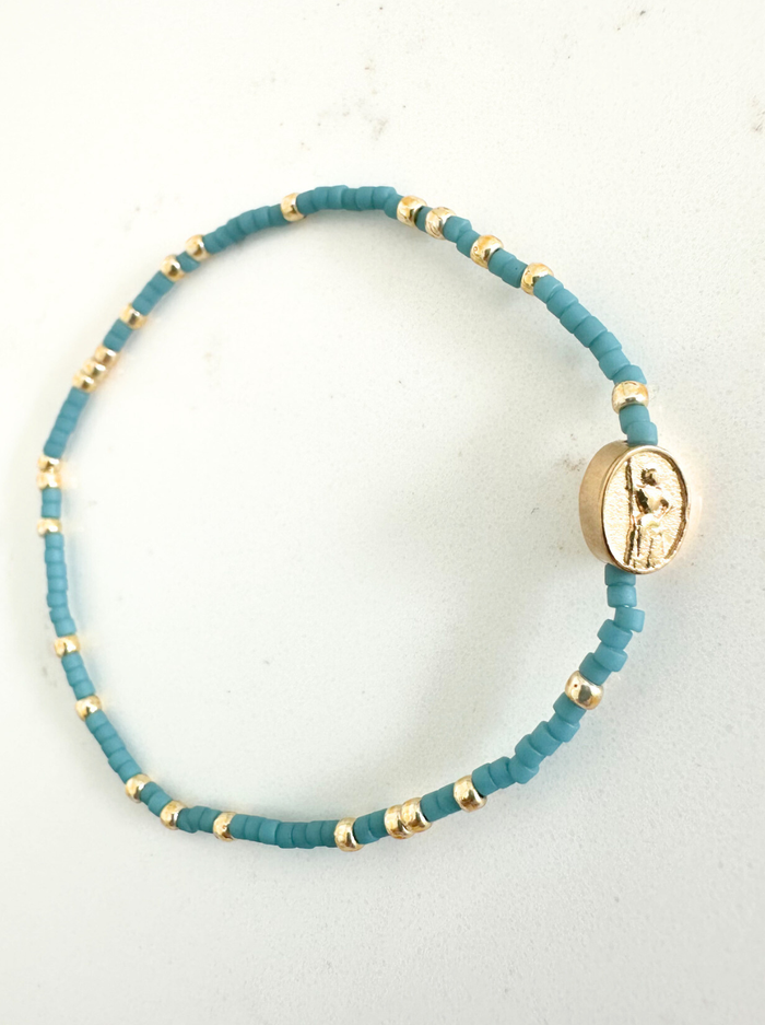 Teal beaded bracelet with gold accents on a white background