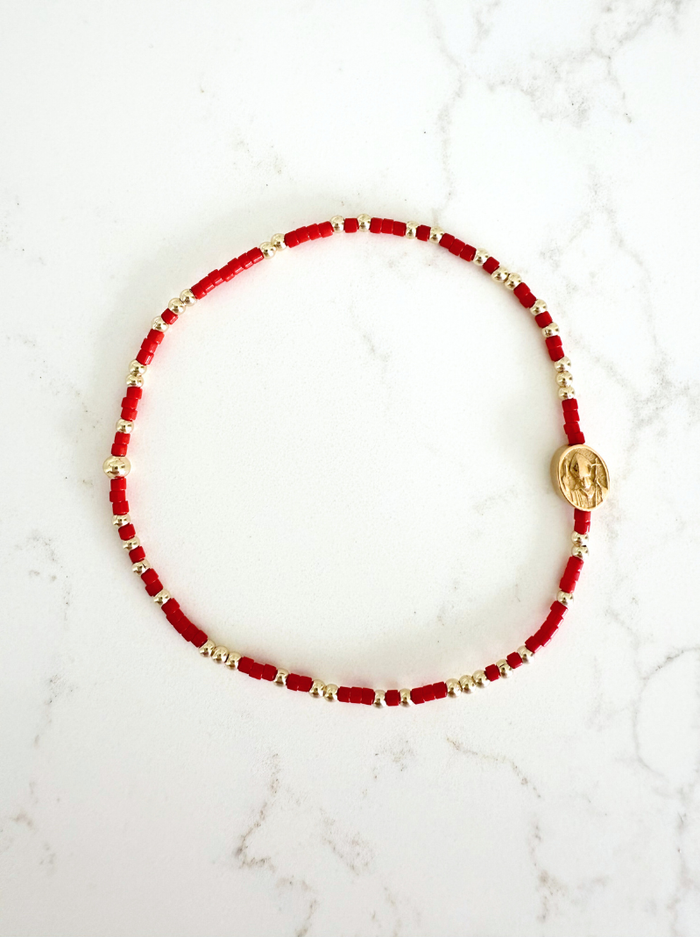 Red beaded bracelet with gold accents on a white marble surface