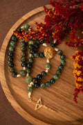 Green beaded rosary with gold accents on a wooden surface with red flowers.