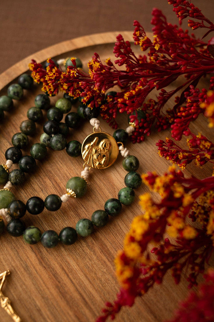 Green beaded rosary with gold charm on a wooden surface with dried flowers.