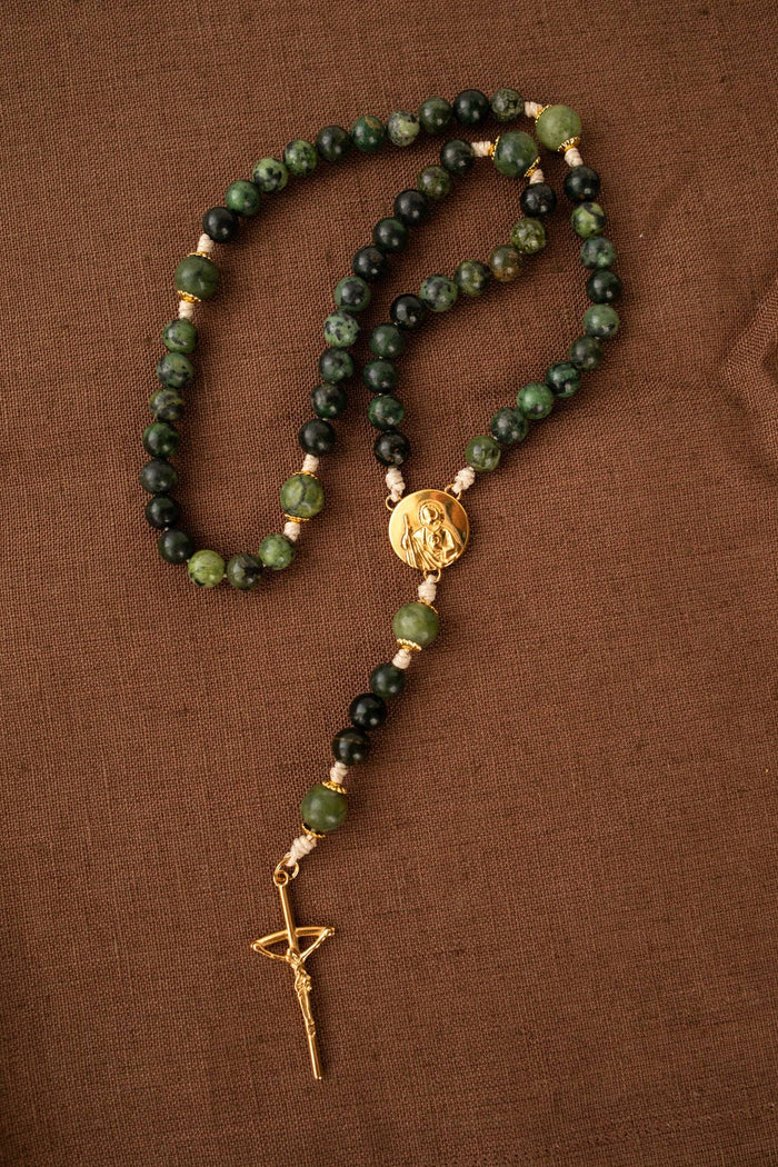 Rosary with green and black beads and a gold cross pendant on a brown fabric background