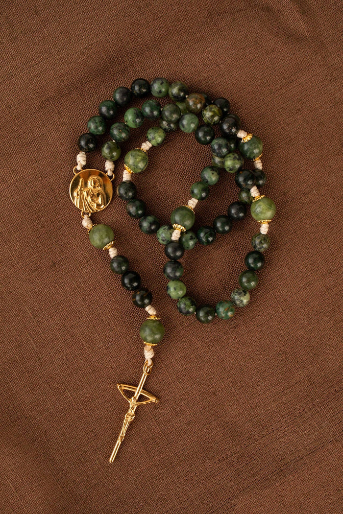 Green and black beaded rosary with gold crucifix on a brown background