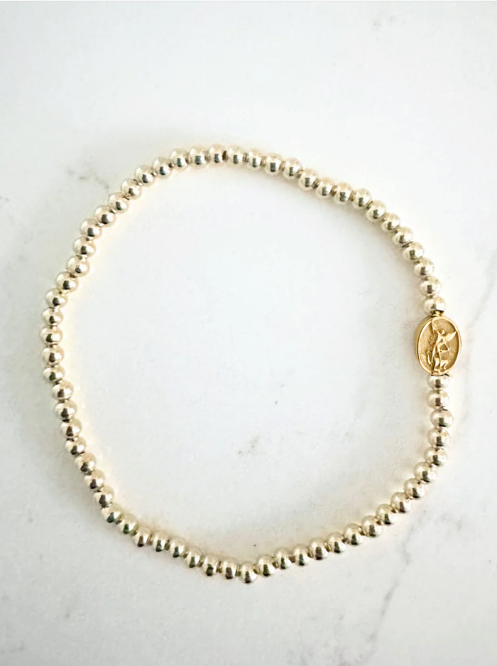 Gold beaded bracelet with a pendant on a white marble surface