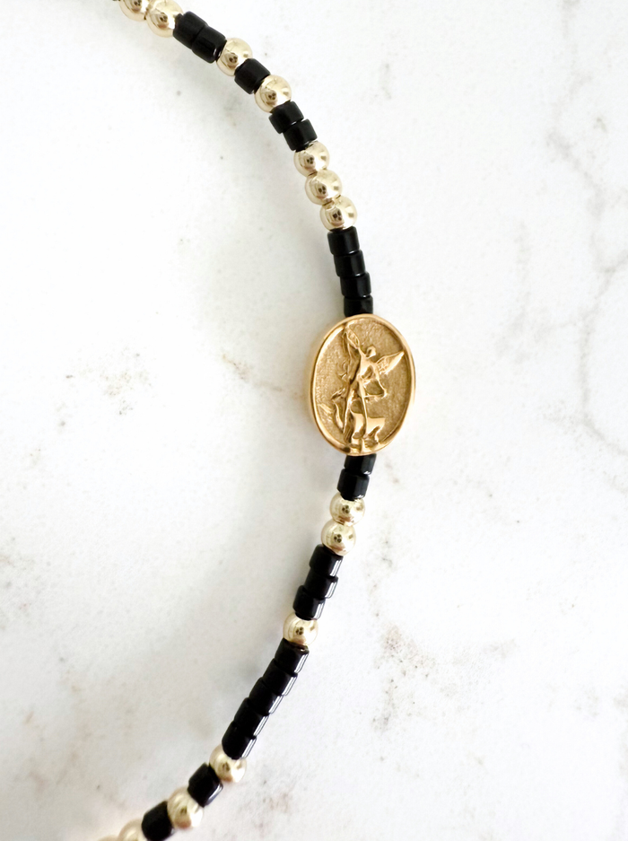 Black and gold beaded bracelet with a pendant on a white marble background