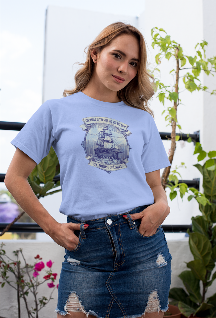 Woman wearing a light blue t-shirt with a graphic design, standing outdoors with plants in the background.