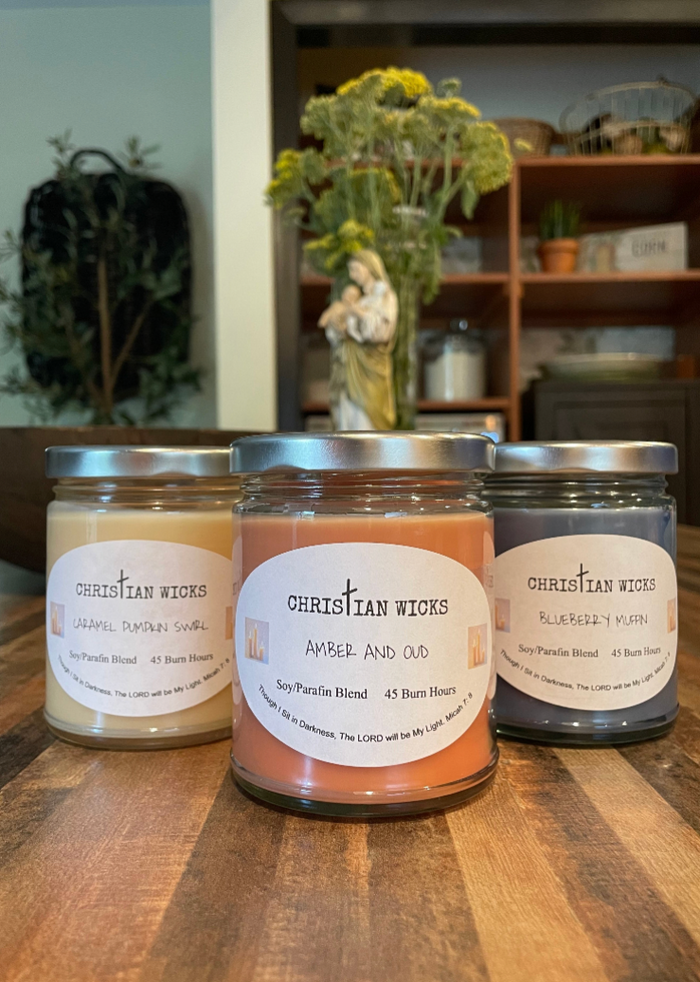 Three candles with labels on a wooden surface, with a blurred indoor background.