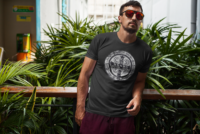 Man wearing a black t-shirt with a logo, standing in front of green plants.