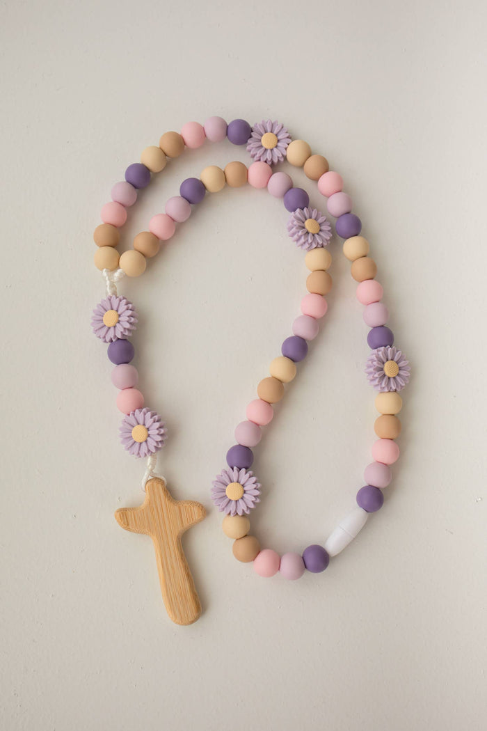 Pastel-colored beaded necklace with wooden cross and flower decorations on a light background