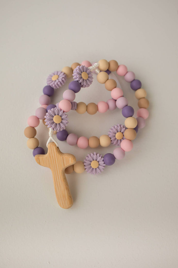 Pastel-colored beaded rosary with wooden cross and floral decorations on a light background